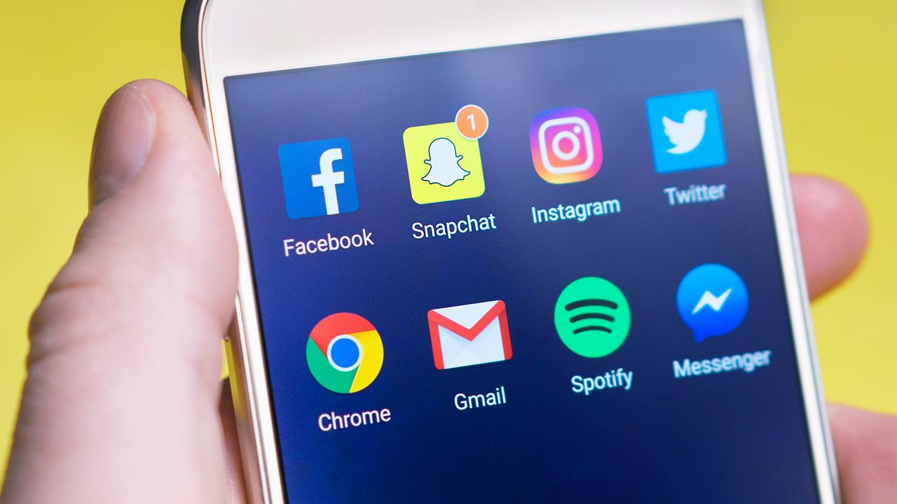 why-choose-us A person's hand holding a smartphone with social media and communication apps on the screen.